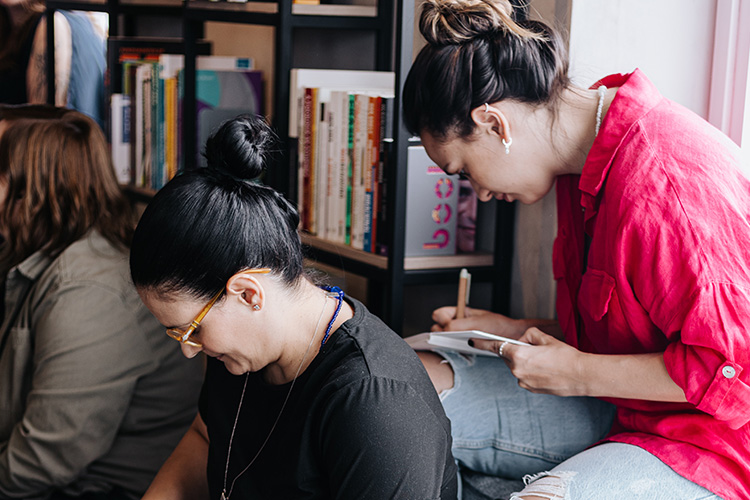 3 mulheres concentradas enquanto preenchem algo relacionado a uma das atividades em andamento.